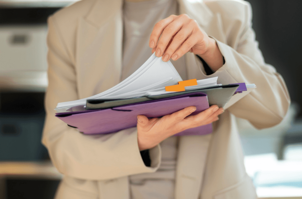 Woman holding printed folders with documents, showcasing organizational tools for effective communication and brand presentation in a professional setting.