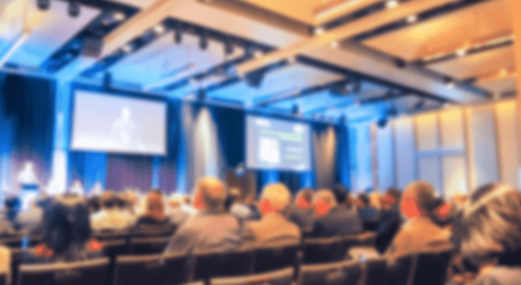 Audience engaged at a business event featuring a presentation on a screen, highlighting the importance of event printing for marketing and brand visibility.